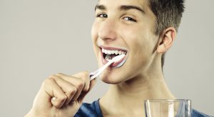 A teenager demonstrating good personal hygiene by brushing his teeth.